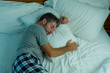 © TheVisualsYouNeed - domestic lifestyle high angle portrait of young attractive and relaxed man sleeping alone on bed at home lying tranquil at night in dim light resting and dreaming