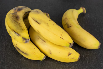 Group of five whole sweet yellow banana on grey stone