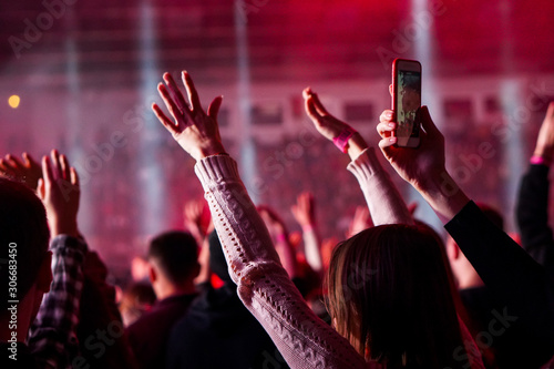 Fototapeta na szkło Publiczność z rękami uniesionymi na festiwalu muzycznym i światłami spływającymi z góry. Miękka ostrość, wysokie ISO, ziarnisty obraz.