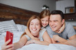 © alfa27 - happy caucasian parents lying on bed together with kid girl, having leisure time together at home
