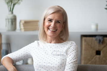 Headshot aged woman smiling sitting on couch looking at camera