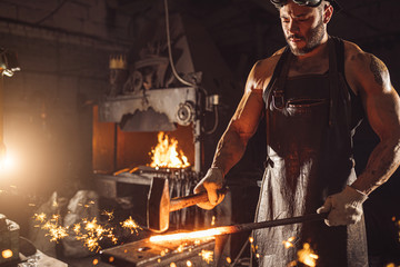 Wall Mural - handsome forger having muscular body beat iron with hammer isolated in dark whorkshop. power and strength