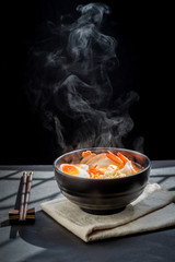 Noodles with steam and smoke in bowl on wooden background, selective focus. Asian meal on a table, junk food concept