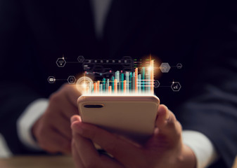 Stock exchange market concept, hand trader holding smartphone with graphs analysis candle line on bokeh colors light in night.