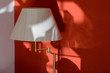 Stehlampe mit Lampenschirm vor roter Wand, mit Schatten durch Sonneneinfall, Ausschnit