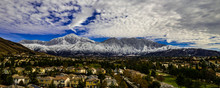 Aerial Panorama Of Snow Covered San Gorgonio And Little San Bernardino Mountains On A Winter Day Above Yucaipa Valley With Blue Sky, White Clouds, Houses, Hills