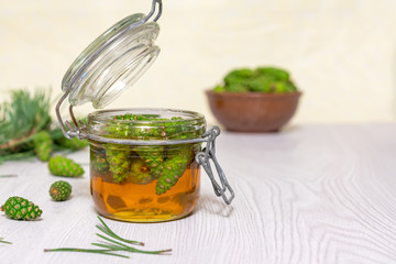 An open glass jar of honey with young green pine cones on a light wooden table. Gourmet Dessert. Natural medicine