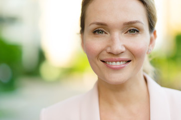 Close-up portrait of a smiling woman on the street. Happy woman's face closeup, outdoors. Happy businesswoman in a light jacket looks at the camera. Urban portrait of a beautiful blonde woman.