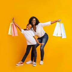 Portrait of cheerful black mom and daughter with colourful shopping bags