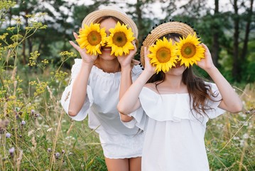 Cheerful mother and her little daughter having fun together in the summer background. Happy family in the nature background. Cute girls with colorful flowers.