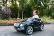 © Serhii - Cute boy in riding a black electric car in the park. Funny boy rides on a toy electric car. Copy space.