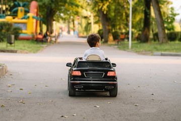 Cute boy in riding a black electric car in the park. Funny boy rides on a toy electric car. Copy space.