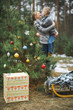 © sofiko14 - Christmas present box, wooden Santa's sledge with Christmas gifts, decorated Christmas tree over the background of winter forest and mother and son hugging. Merry Christmas and Happy New Year Concept.