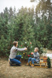 © sofiko14 - Pretty young mother and the son in gray sweaters decorating a Christmas tree in winter forest outdoors. Boy is drinking hot tea and sitting on wooden sledge with present boxes under the tree
