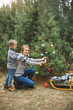 © sofiko14 - Mother and little son looking at camera and smiling, while decorate Christmas tree in winter forest, outdoors. New Year decorations, wooden sledge, present gifts