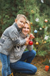 © sofiko14 - Family, young mother and little son, wearing knitted sweaters, decorating fir tree in the forest or park. Colorful decorations, Christmas presents