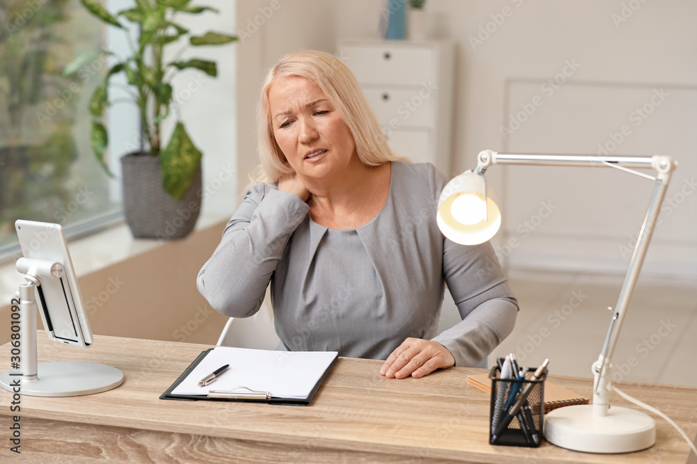 Mature woman suffering pain in neck at workplace