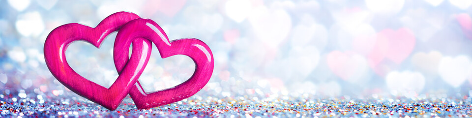 Wall Mural - banner of two wooden interlocked hearts with colorful heart bokeh background - valentine's day/marri
