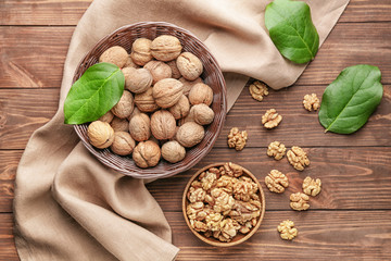 Basket and plate with tasty walnuts on wooden background