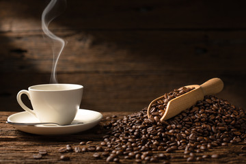 Cup of coffee with smoke and coffee beans on old wooden background