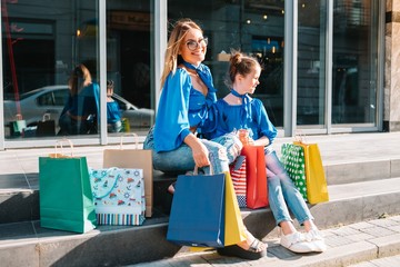 sale, consumerism and people concept - happy young women her dauther with shopping bags walking city street