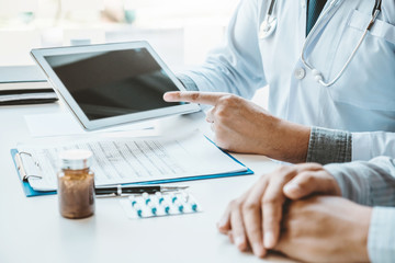 Wall Mural - Doctor consulting with patient presenting results on digital tablet tablet sitting at table