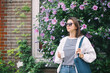 © papa - A happy young woman in sunglasses and with a paper Cup of coffee stands at a flowering Bush on the street of the summer city.