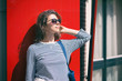 © papa - Portrait of a young woman in sunglasses on a background of red window shutters.