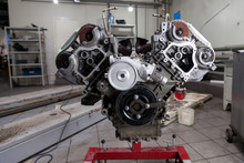 Used v8 engine mounted on a crane for installation on a car after a breakdown and renew in a vehicle repair workshop as a guarantee for the dealership. Auto service industry.