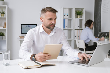 Wall Mural - Confident businessman with tablet sitting by desk in front of laptop