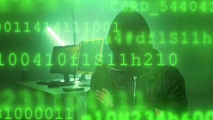 Hacker with masked face working on a computer for cyber attack while green binary hacking code characters running in front of him in a dark room. Augmented reality 4K (UHD)