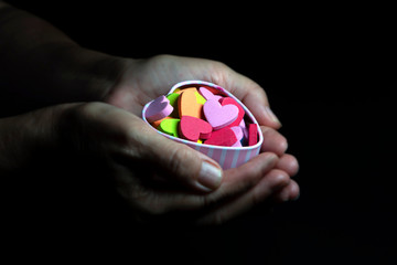 Colorful hearts in hands on black background, love concept