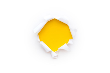 A round hole in white paper with torn edges isolated on a white background with a bright yellow color paper background inside.