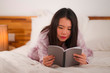 © TheVisualsYouNeed - young beautiful and sweet Asian Korean woman in bed reading book novel feeling happy and relaxed or studying at home wearing cute pajamas cozy and homey