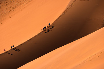 aerial view group of traveler walking on the sand dune in the desert and sun gradually create beauti