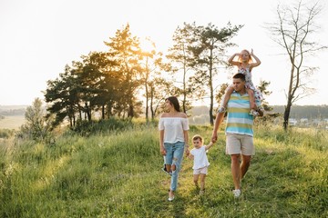 Color photo of smiling young parents and two children, rest and have fun in nature. Love, family and happy childhood lifestyle concept