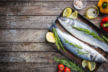 Canvas Print - Fresh raw seabass and ingredients for cooking. Two fish seabass with lemon, spices and herbs on wooden table, top view with copy space.