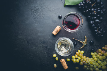 Glasses of white and red wine with ripe grapes on black stone background, top view