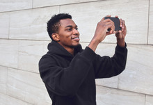 Young Smiling African Man Taking Selfie Picture By Phone On City Street Over Gray Wall Background