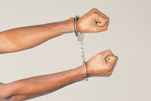 Close-up Hands Arrested African Man. African Hands In Handcuffed Isolated On Gray Background. Prisoner Or Arrested Terrorist Hands In Handcuffs 