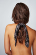 © RedUmbrella&Donkey - Close-up back shot of a brunette lady with a black satin hair scarf fixed on the scrunchie with white Paisley print. The shirtless woman with a ponytail is posing on the gray background.