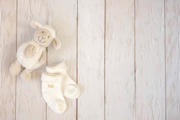 Baby socks and toy lamb on light wooden background. Motherhood concept. Top view, flat lay composition. Copy space for text.