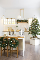 Christmas decor. Bright interior of white kitchen with decorated Christmas tree, garlands and Christmas wreaths.