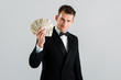 © LIGHTFIELD STUDIOS - happy and rich man in suit holding dollar banknotes isolated on grey