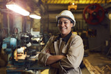 Fototapeta  - Waist up portrait of mixed-race female worker posing confidently while standing with arms crossed in factory workshop