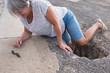 mature woman or senior walking in a building zone and falling in a big hole with her leg inside it - needing help on the ground with ache