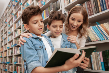 Lovely family looking excited and overwhelmed, reading a book at the library. Twin brothers and their mom at the library or bookstore