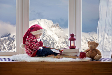 Canvas Print - Sweet blonde child, boy, sitting on window shield with teddy bear friend toy, writing letter to Santa Claus and reading book