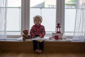 Canvas Print - Sweet blonde child, boy, sitting on window shield with teddy bear friend toy, writing letter to Santa Claus and reading book