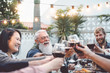 © Alessandro Biascioli - Happy family dining and toasting red wine glasses outdoor - People with different ages and ethnicity having fun in barbecue dinner party - Parenthood youth and elderly weekend activities concept